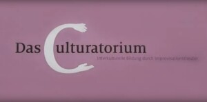 Das Bild ist ganz in Lila gehalten. Auf dem lila Hintergrund steht mit schwarzer Schrift geschrieben Das Culturatorium - Improvisionstheater für interkulturelle Pädagogik. Das C ist dabei sehr viel größer gehalten als alle anderen Buchstaben, mit weißer Farbe geschrieben und dessen beide Enden werden zu Händen