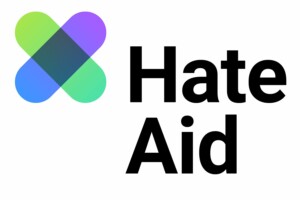 Auf dem Bild steht Hate Aid. Daneben ein Logo, dargestellt als X mit unterschiedlichen Farben. Das Bild wird für den Beitrag Journalismus in Gefahr? verwendet