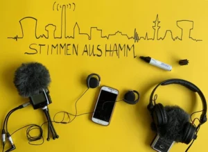 Das Bild ist gelb und es ist die Skyline von Hamm mit einem Edding aufgemalt. Unter der Skylineliegt ein Mikrofon, ein Handy und Kopfhörer.